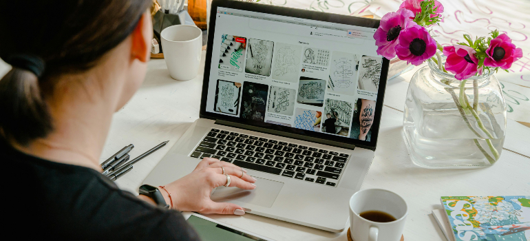 Person working on a laptop with product images, focusing on optimizing your E-Commerce site for conversions. Desk includes flowers and coffee.