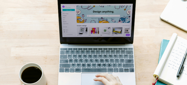 A person working on a laptop with a design software open, while holding a cup of coffee.