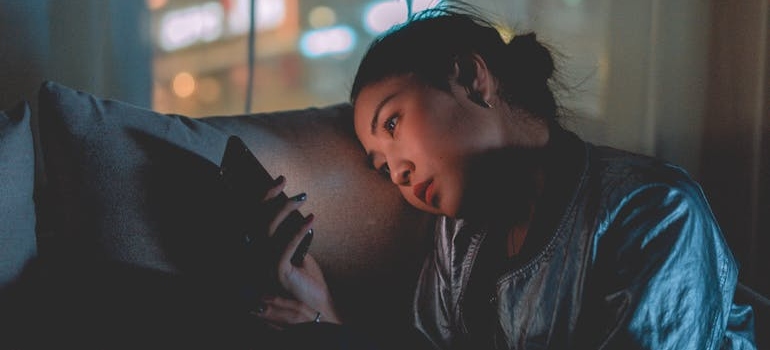 A person sitting alone in the dark and looking at their phone