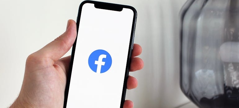 A person holding a phone with the Facebook logo on the screen