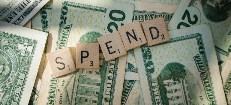 Dollar bills with scrabble tiles spelling “spend”