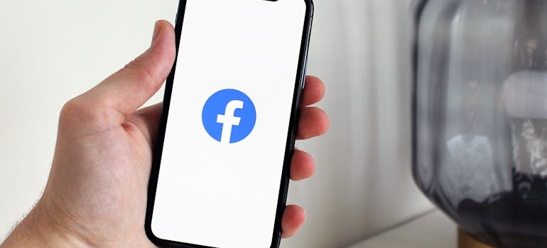 A person holding a phone with the Facebook logo on the screen