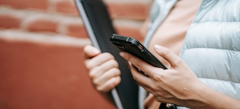 A person using a smartphone and holding a laptop