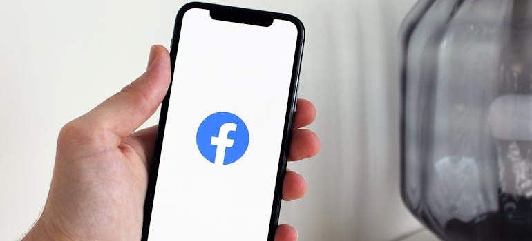 A person holding a smartphone displaying the Facebook app icon on the screen